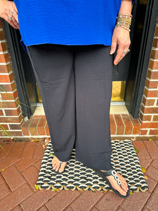 A person wearing comfortable black crinkle textured wide-leg palazzo pants and a bright blue top, standing on a decorative doormat.